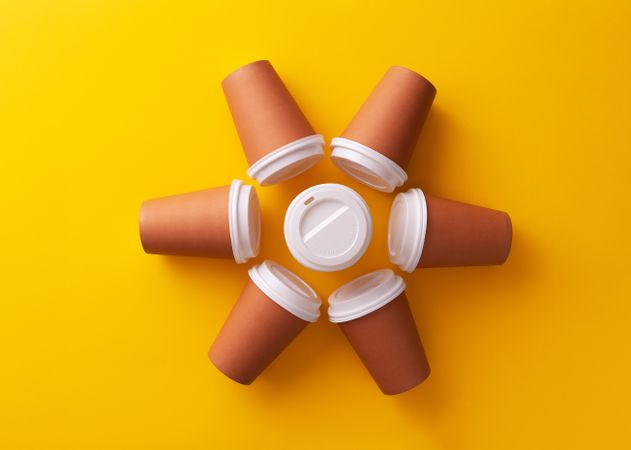 Disposable coffee cups on yellow background in sun shape