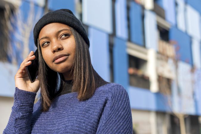 Female in wool hat and blue sweater chatting on phone and looking to the side