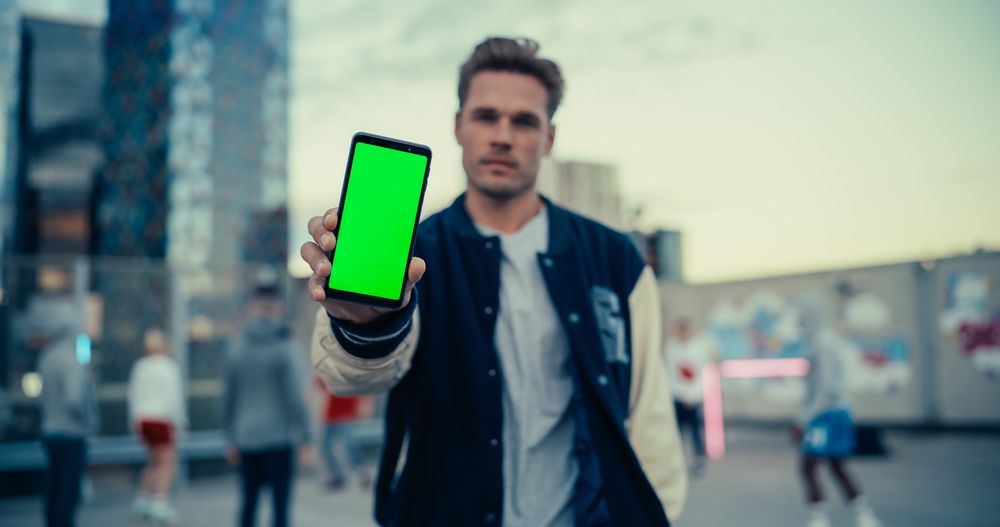 Man Holding a Smartphone, Showing the Green Screen Mock Up Display.