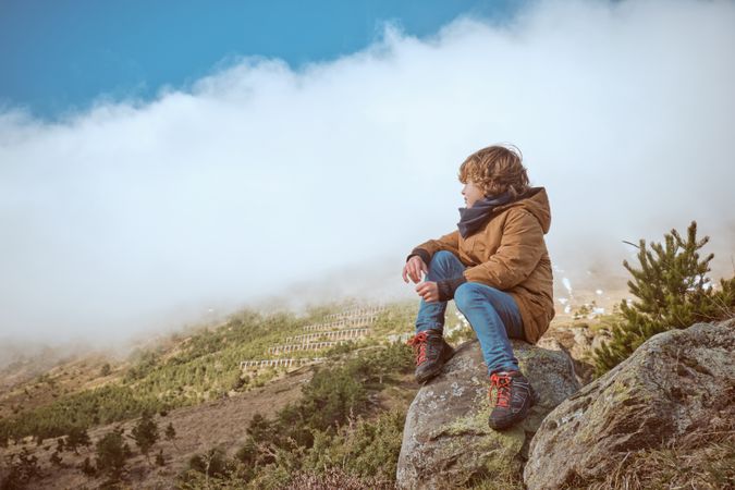 Boy in warm clothes observing nature from boulder