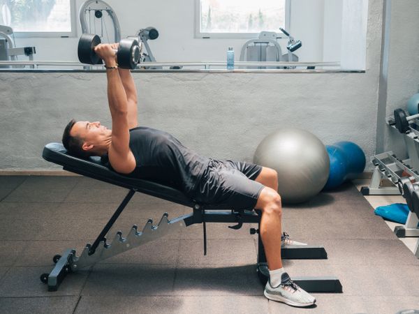 Strong man exercising with dumbbells on bench