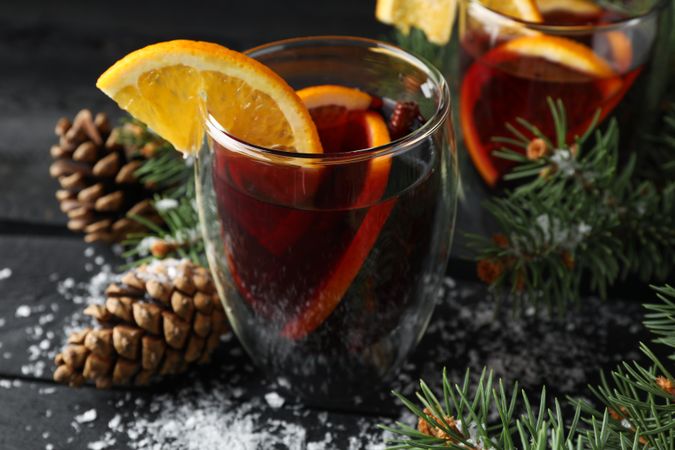 Glasses of tasty mulled wine with orange on decorated wooden background, close up