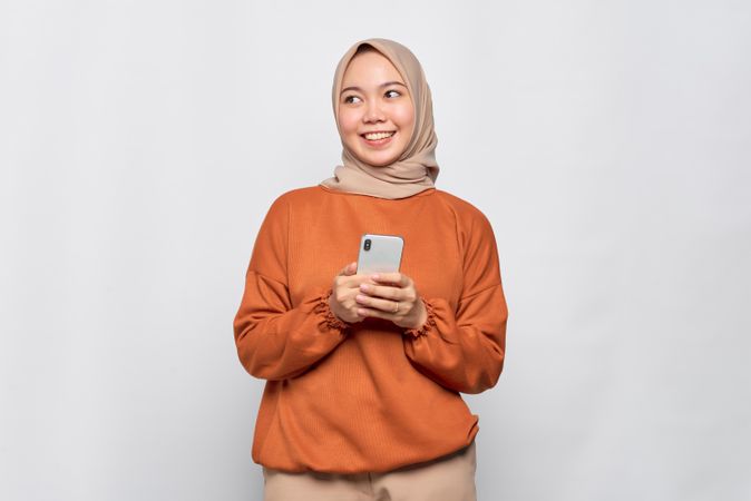 Calm Muslim woman in headscarf and orange shirt holding phone