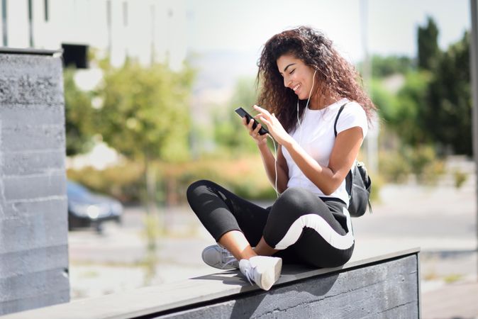 Arab woman texting on phone and smiling sitting outdoors