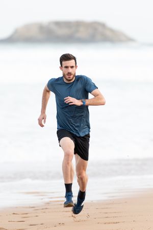 Sportsman in active wear jogging on lonely beach