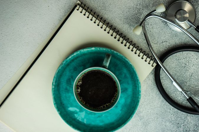 Coffee in teal cup with phone, stethoscope and notepad