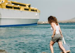 Curly woman looking at ship in water on seashore