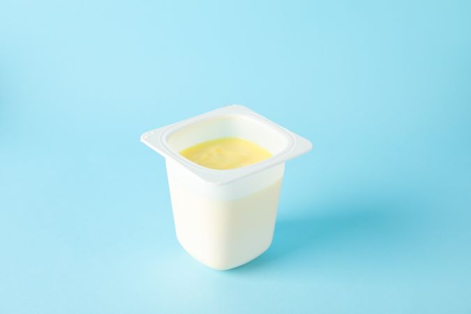 Plastic cup with yogurt on color background, space for text