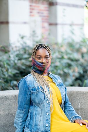 Portrait of woman with mask and long braids sitting outside smiling and looking at camera