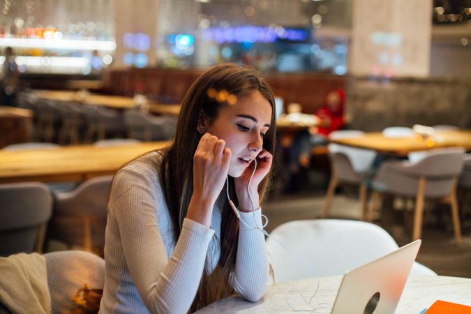 Brunette woman in a restaurant working on her laptop with earbuds