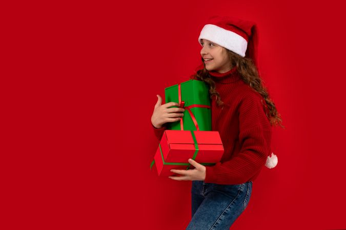 Girl in Santa hat holds presents and looks aside