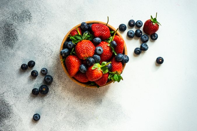 Top view of summer berries in wooden bowl full on grey counter with copy space