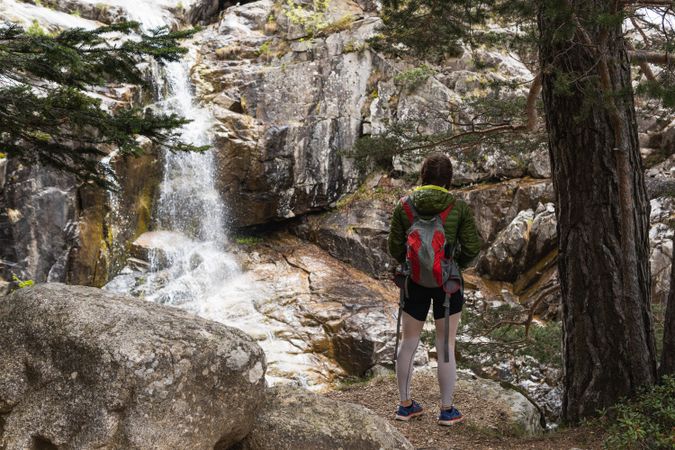Unrecognizable female hiker standing near waterfall in mountainous forest