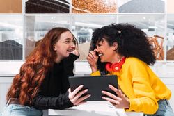 Positive multiethnic female friends using tablet and laughing in cafe