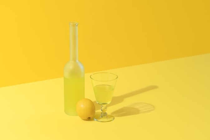 Lemon liqueur bottle and glass on a yellow background