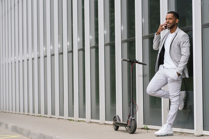 Elegant Black man talking smartphone leaning building