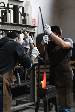 Workers in protective googles and apron working in forge
