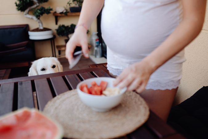 Faceless pregnant woman cutting watermelon to bowl