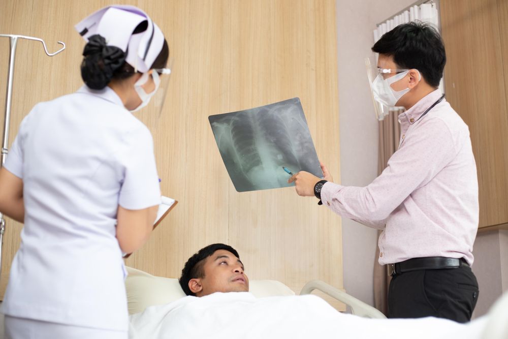 Patient lying in hospital bed with medical professionals showing chest X-ray