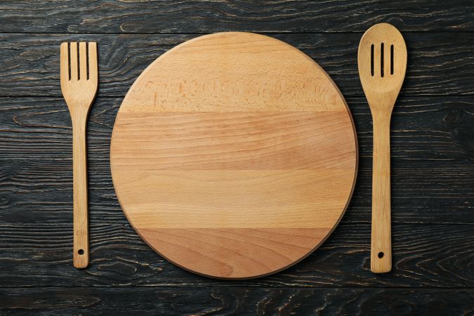 Wooden cutlery and round cutting board on wooden background