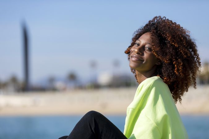 Confident female sitting near ocean in bright green shirt