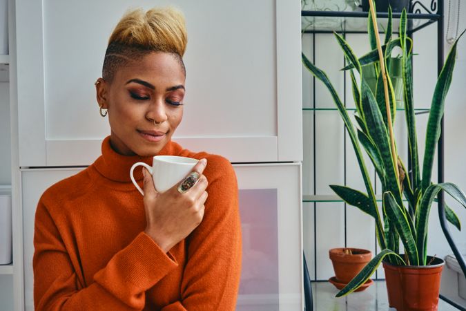 Black woman with her eyes closed with coffee mug in a bright home