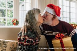 Man in santa cap kissing his wife holding a christmas present 5oEjxb