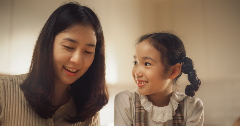 Portrait of a Happy Korean Mother and Cute Daughter at Home, Smiling and Looking at Eachother.