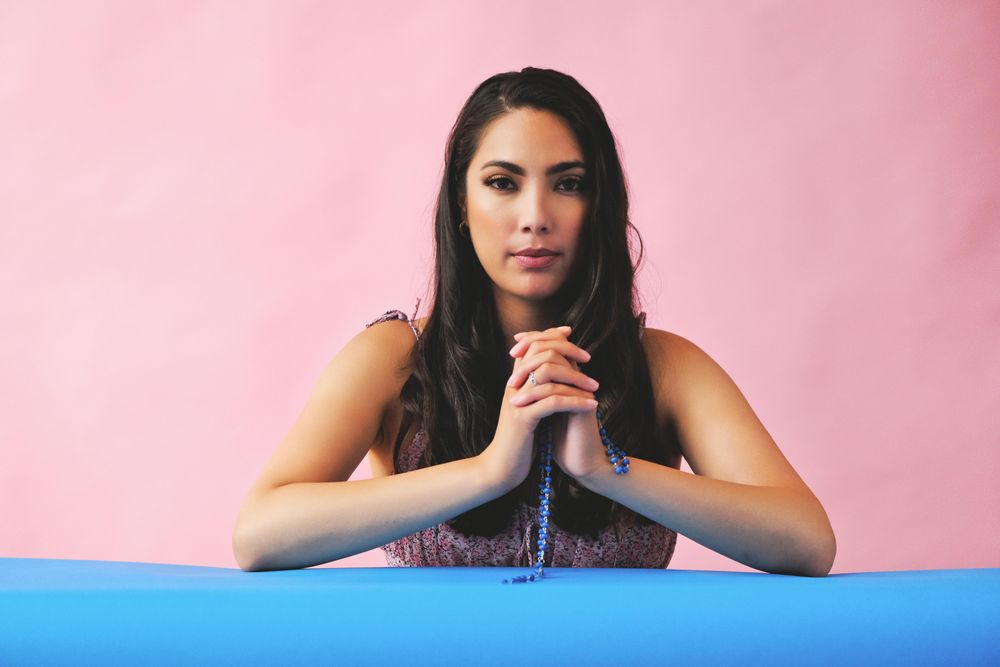 Hispanic woman praying with rosary beads in pink room