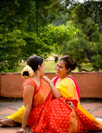Two women in sarees sitting on green grass outdoor