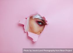 Female with eye makeup peeking through torn paper 5RV3L2