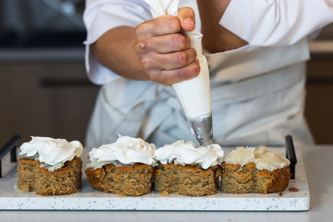 Crop baker decorating carrot cakes with cream