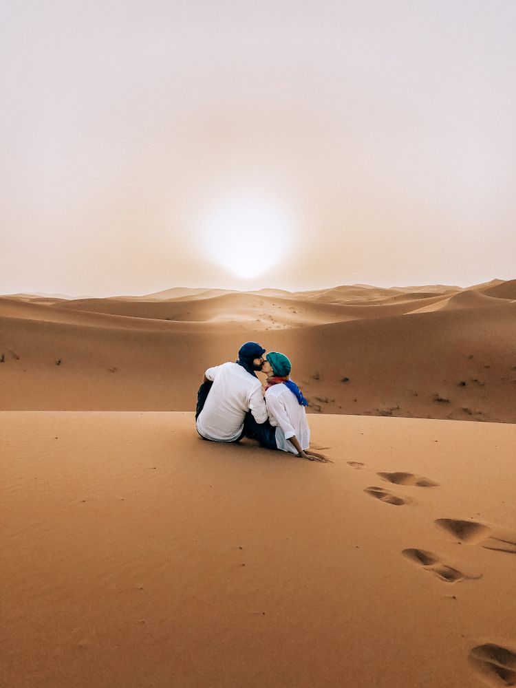 Back view of man and woman kissing and sitting in Moroccan desert