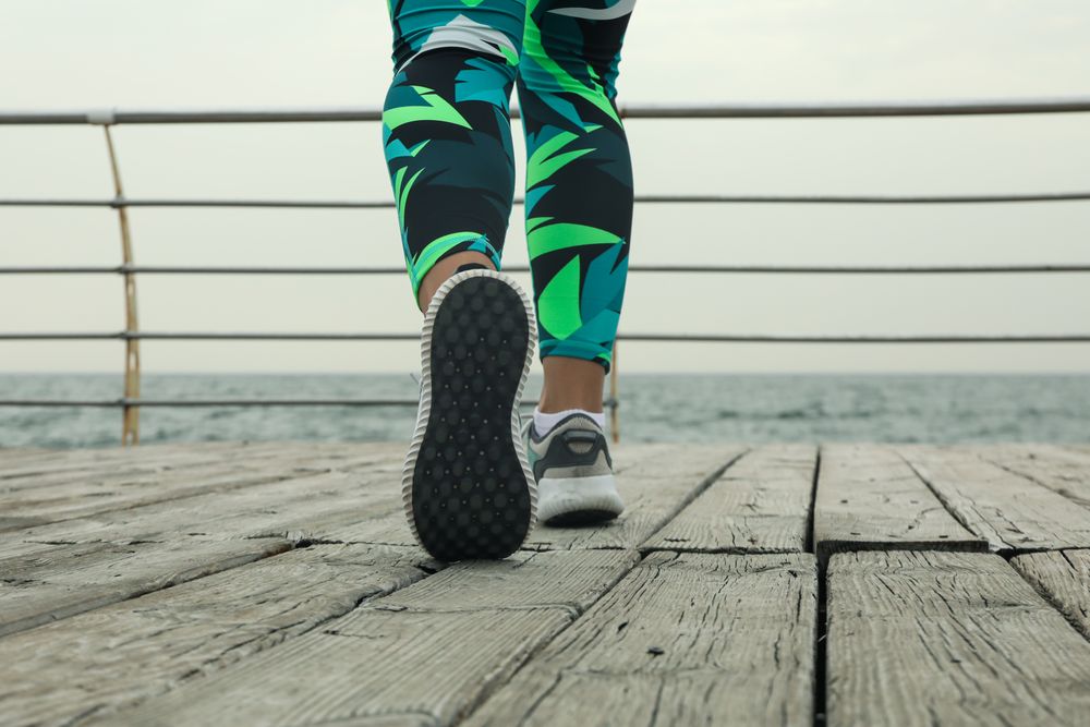 Female legs in bright leggings and sneakers on wooden floor outdoors, close up
