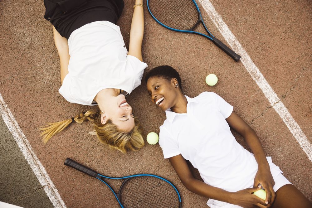 Portrait of two women laying on a tennis court.