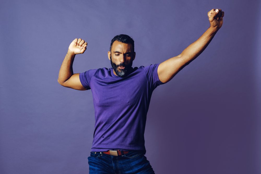 Proud smiling male raising his arms in celebration in purple studio, copy space