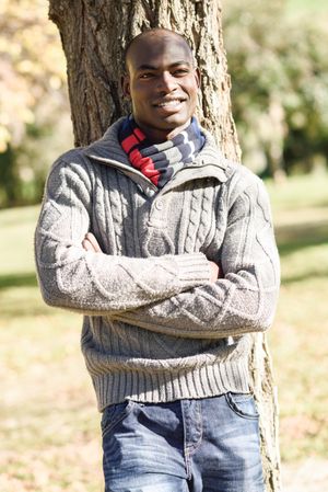 Smiling male in woolen sweater standing in front of trees in park