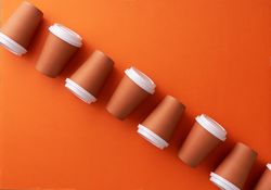 Diagonal row of disposable coffee cups on orange background