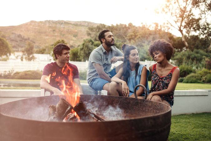 Two young couples sitting in backyard with camp fire