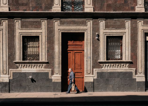 Side view of an older man walking past grand wooden door in Mexico City