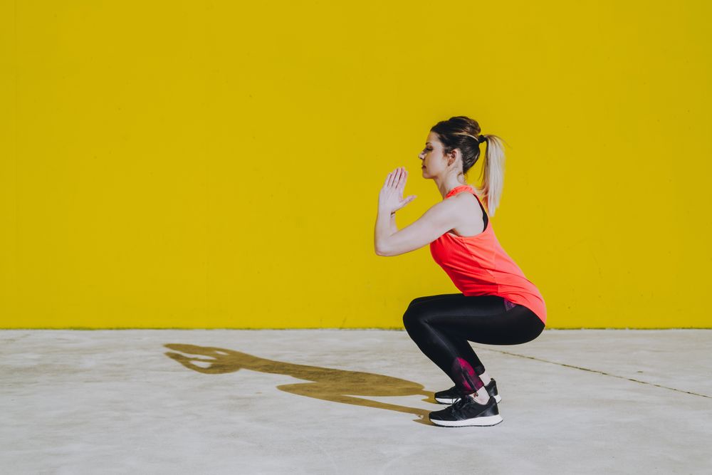 Woman doing squads exercises near a yellow wall