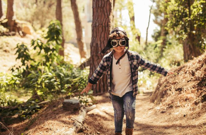 Child with pilot goggles and hat running outdoors in forest