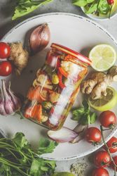 Close up of preserve jar with various pickled vegetables on plate with ingredients