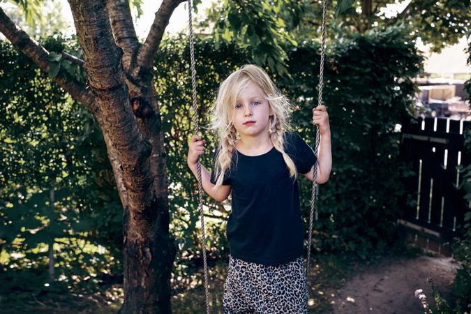 Blonde girl with braided hair standing on outdoor swing