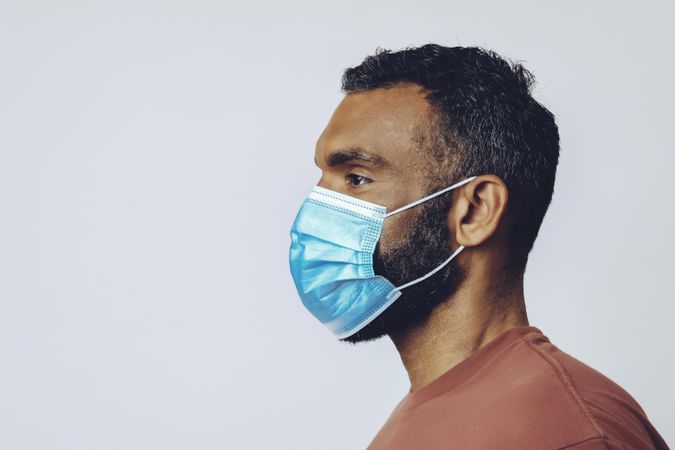 Profile of male looking away from camera wearing medical face mask in studio shoot, copy space