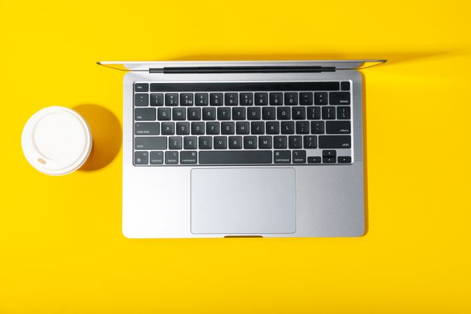 Top view of open laptop with to go cup on yellow desk