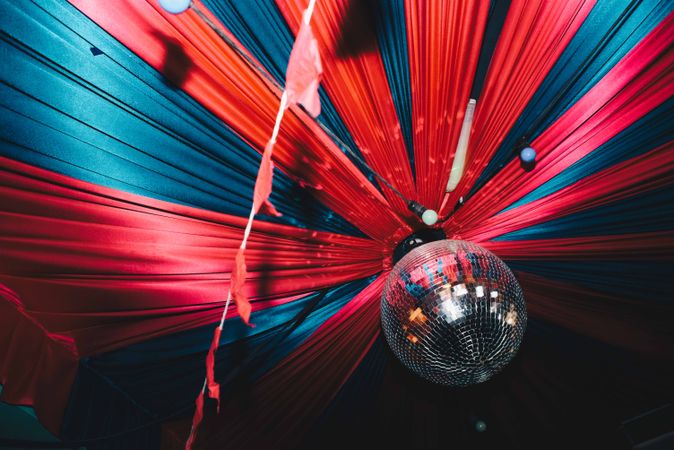 Disco ball hanging from striped fabric tent with pendant banners