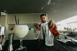 Barman pouring cocktail and alcoholic drinks to shaker in a bar.