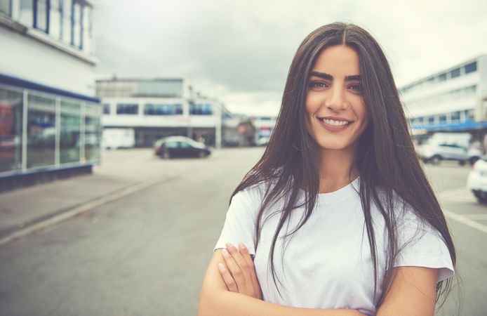 Portrait of content brunette woman standing outside in parking lot
