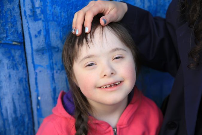 A young girl with Down syndrome smiling with a loving hand on her head